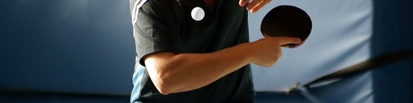 Tischtennisspieler in Aktion, schl&auml;gt einen Ball mit einem Schl&auml;ger auf einem Tischtennistisch.