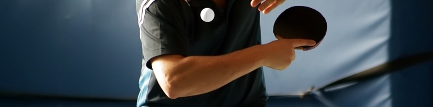 Tischtennisspieler in Aktion, schlägt einen Ball mit einem Schläger auf einem Tischtennistisch.