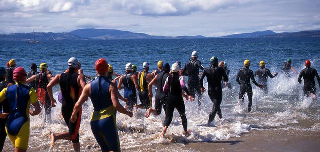 Gruppenswimmer in Neoprenanzügen laufen ins Wasser, um an einem Wettkampf teilzunehmen, bei bewölktem Himmel.