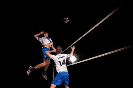 Ein Volleyballspieler springt hoch, um einen Ball zu schlagen, während ein anderer Spieler bereitsteht.