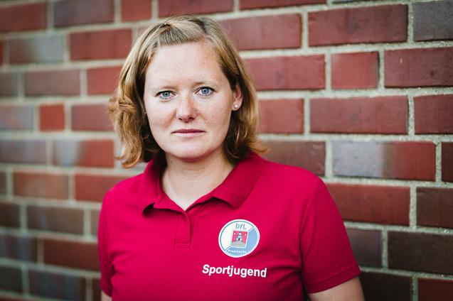Portrait einer person in rotem Poloshirt mit Aufschrift &bdquo;Sportjugend&ldquo; vor einer Ziegelwand.