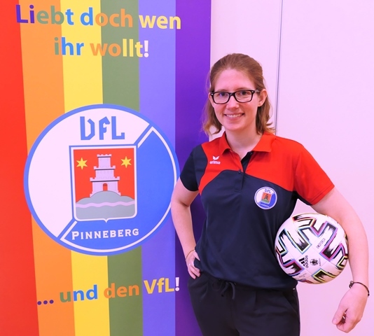 Frau mit Brille und Fußball steht vor einem bunten Banner mit dem Logo des VfL Pinneberg.