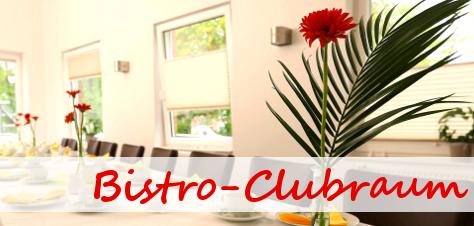 Blick in einen hellen Bistro-Clubraum mit Tisch, Blumen und Stühlen entlang der Wände.