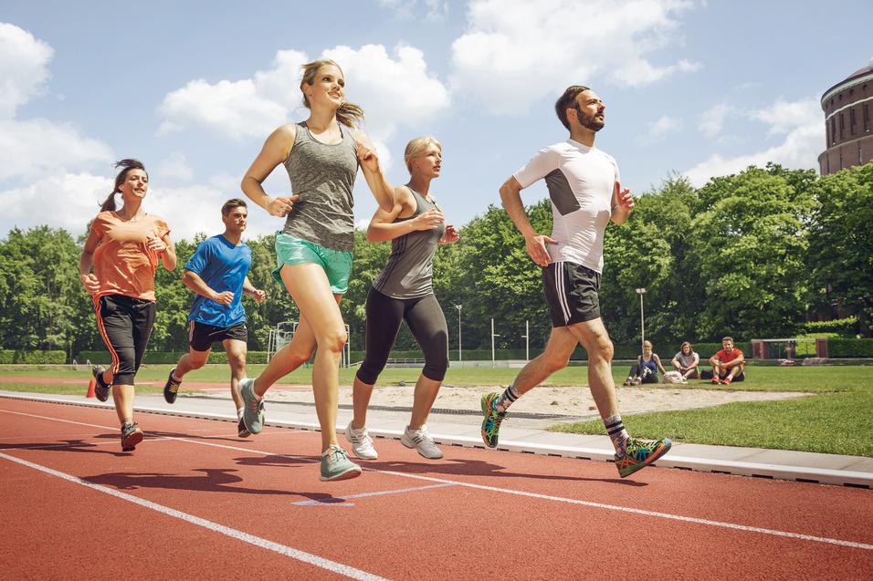 Fünf Erwachsene laufen gemeinsam auf einer Laufbahn im Stadion bei Sonnenschein.